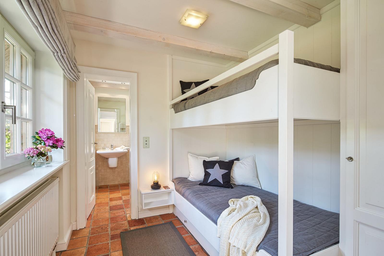 Bedroom with bunk bed, window, and view into the bathroom.