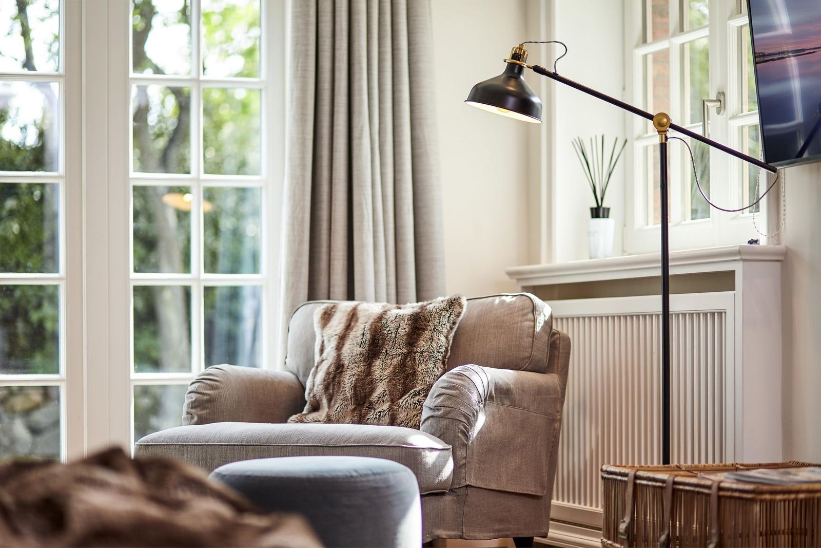 An armchair with a fur cushion is positioned in front of a window with curtains.