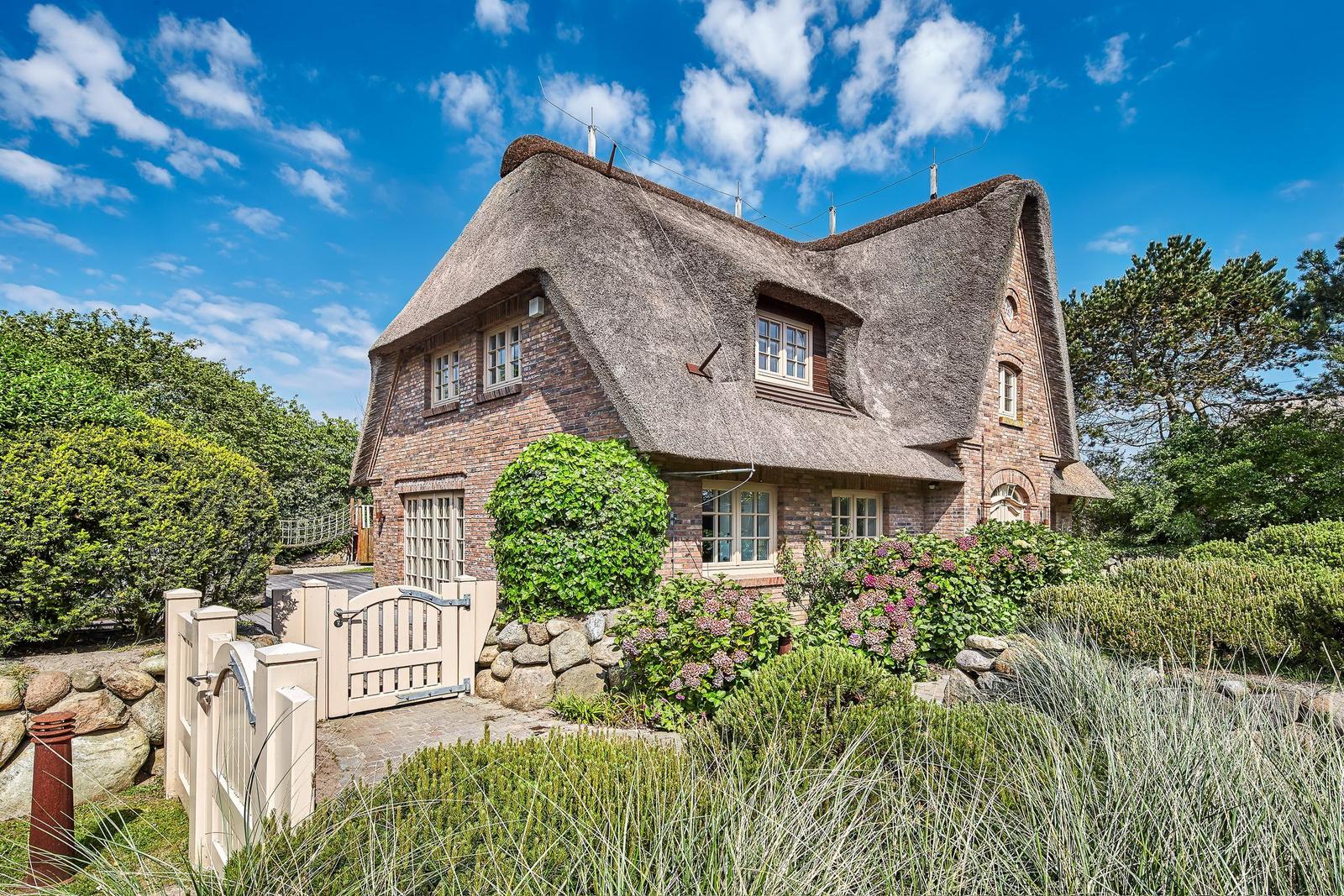 House with thatched roof, stone wall, and garden with flowers.