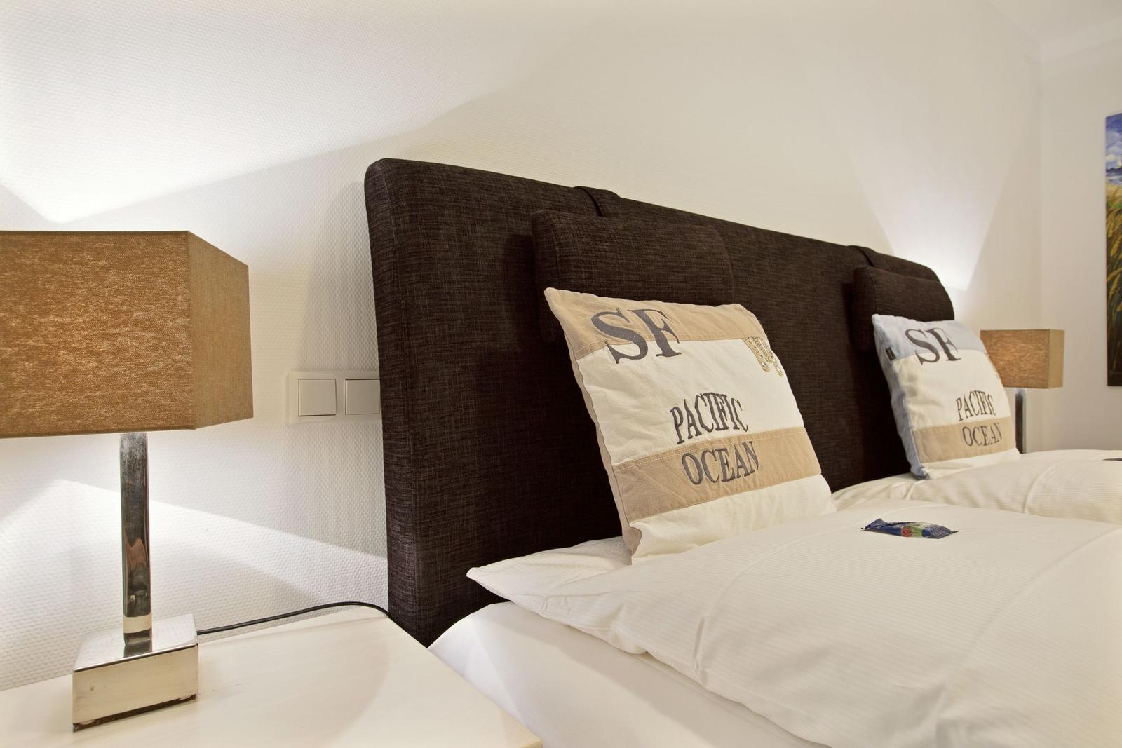 Schlafzimmer mit Bett, Kissen und Nachttisch mit Lampe.