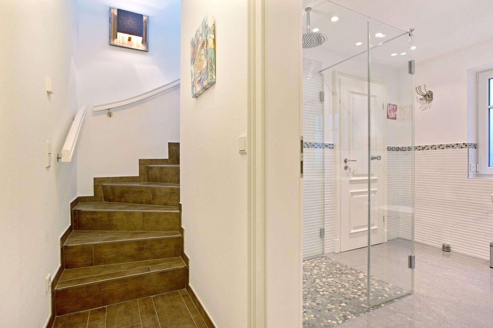 Treppenhaus mit Holztreppe und angrenzender Dusche mit Glaswand.