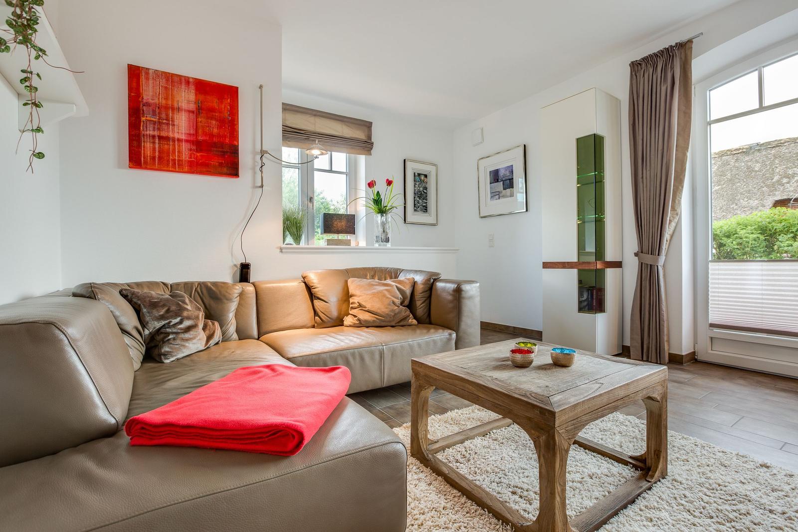 Ein Wohnzimmer mit braunem Ledersofa, Holztisch und Fensterblick.