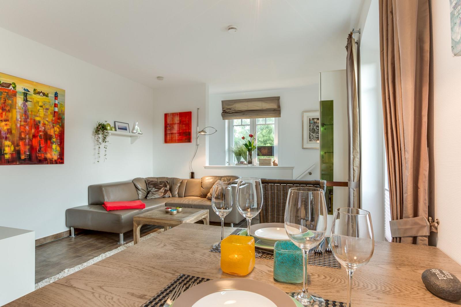 Essbereich mit Tisch, Gläsern und Stühlen. Wohnbereich mit Sofa und Wandbildern.