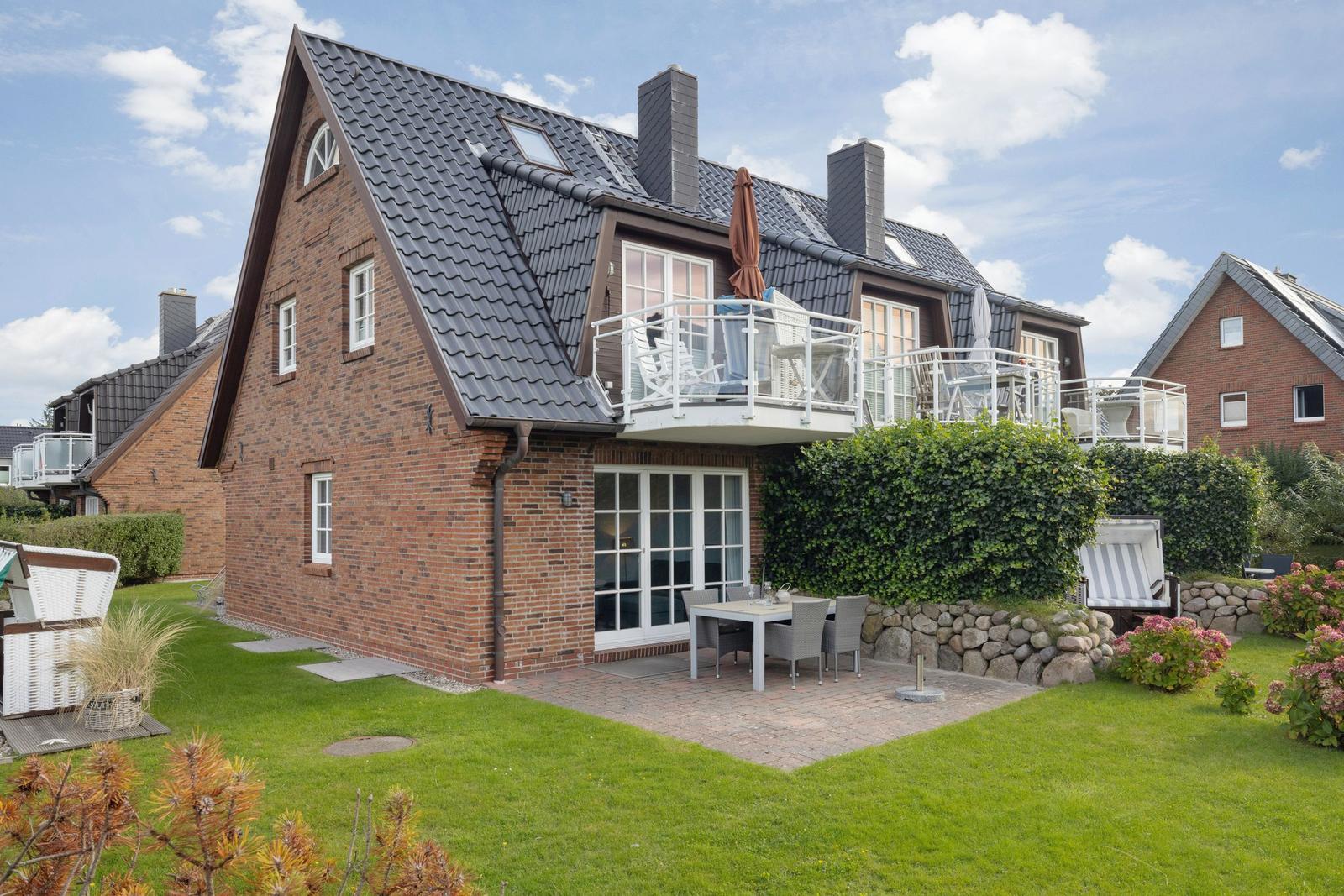 House with balcony, terrace, and garden. Modern design with red brick and dark roof.