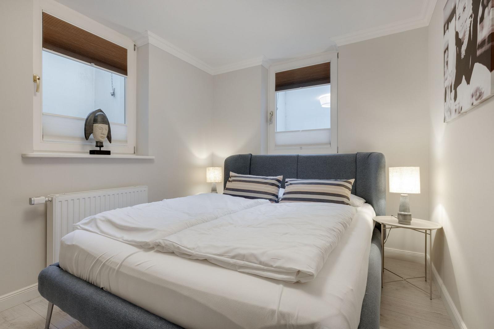 Bedroom with double bed, two windows, and nightstands.