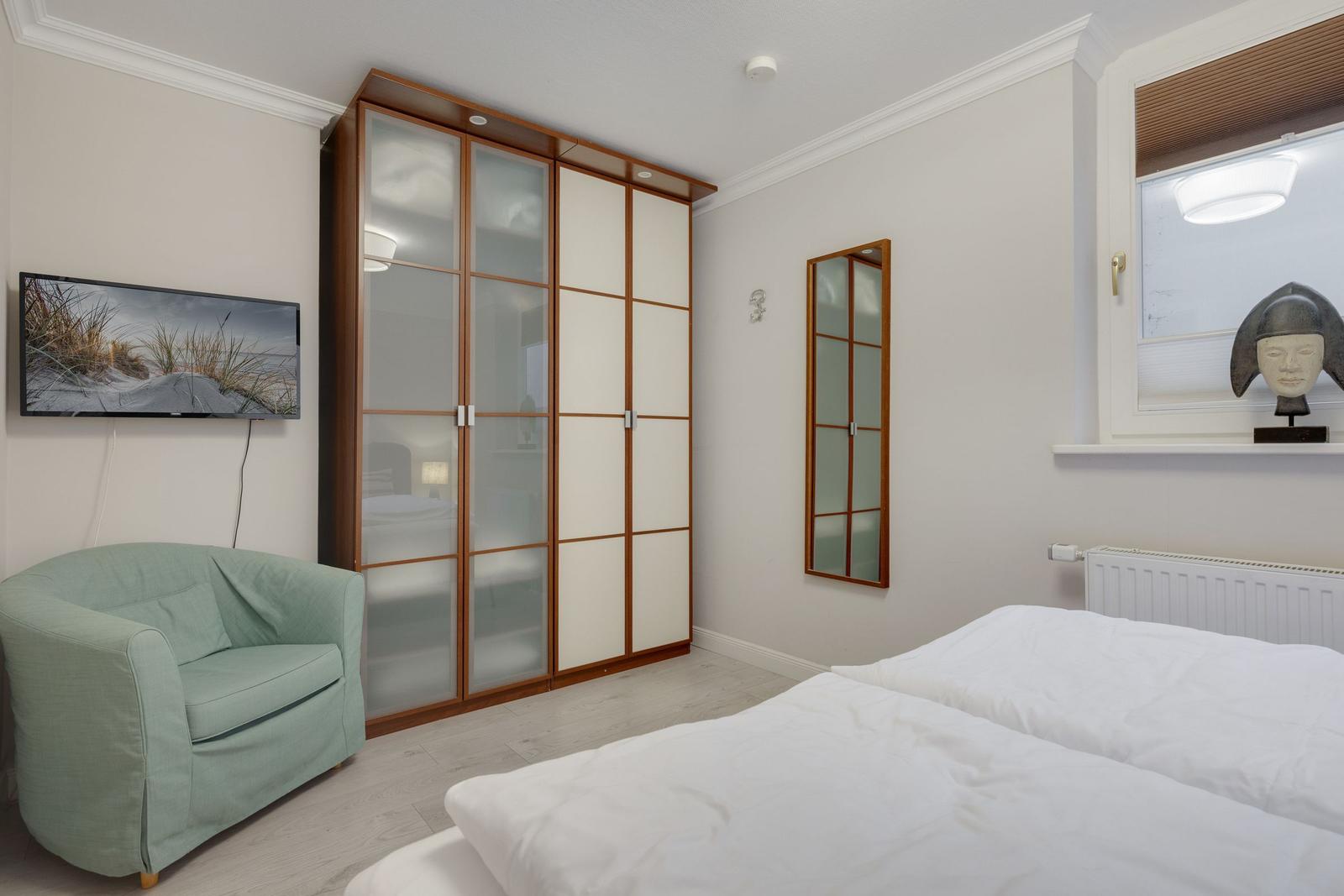 Bedroom with bed, wardrobe, armchair, and TV mounted on the wall.