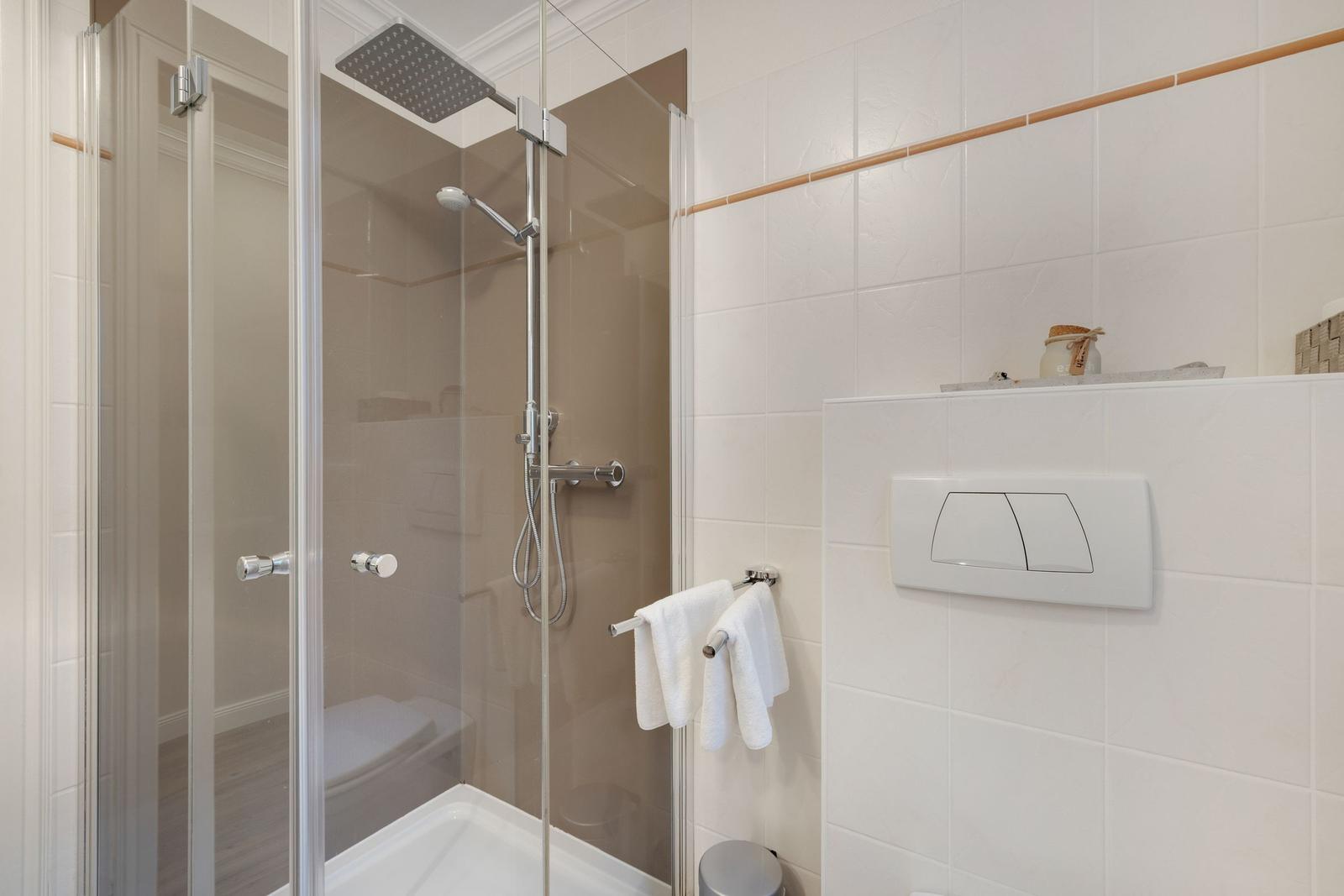 Shower with glass enclosure and shower head, white tiles and towels