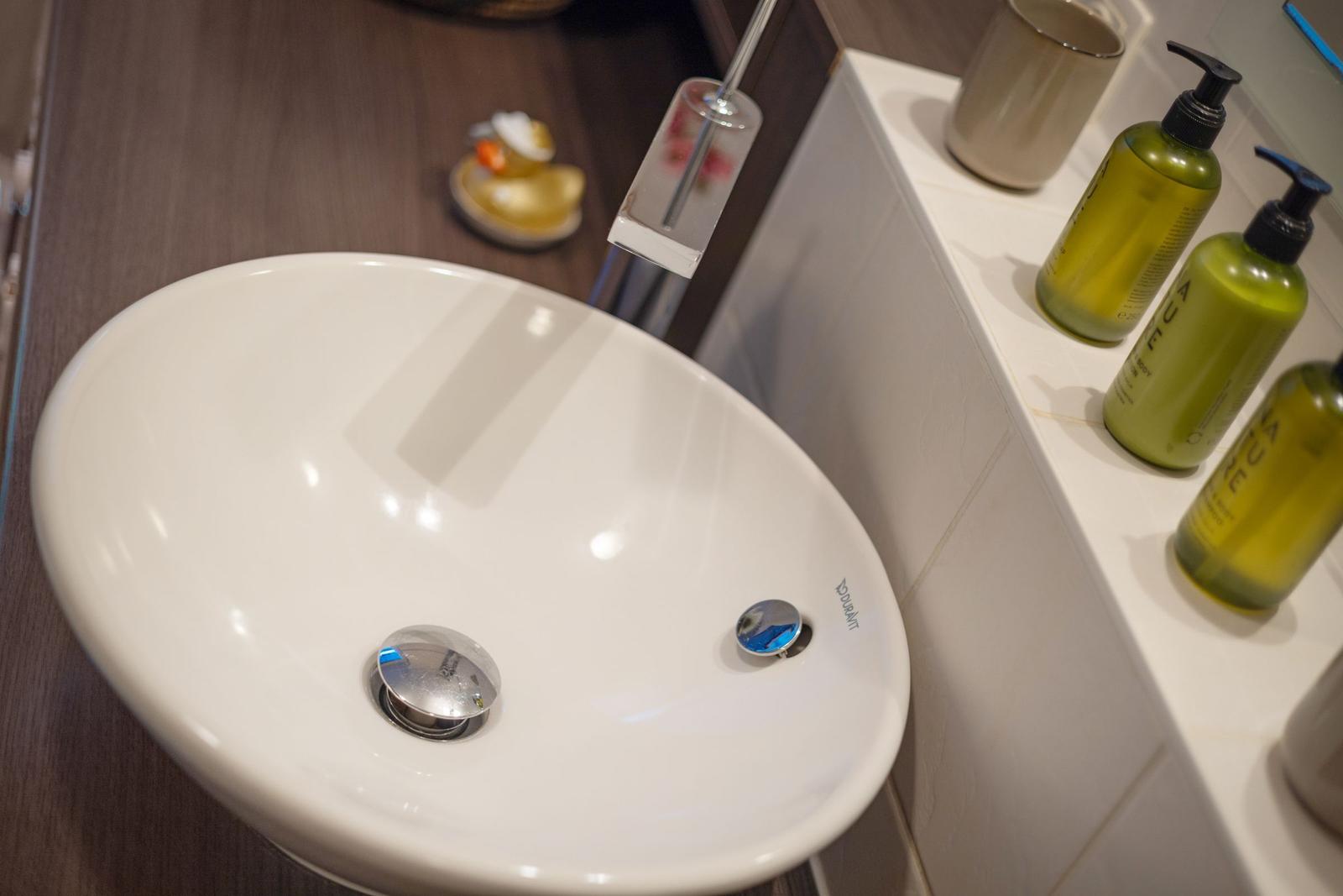 Sink with modern faucet and green bottles on countertop.