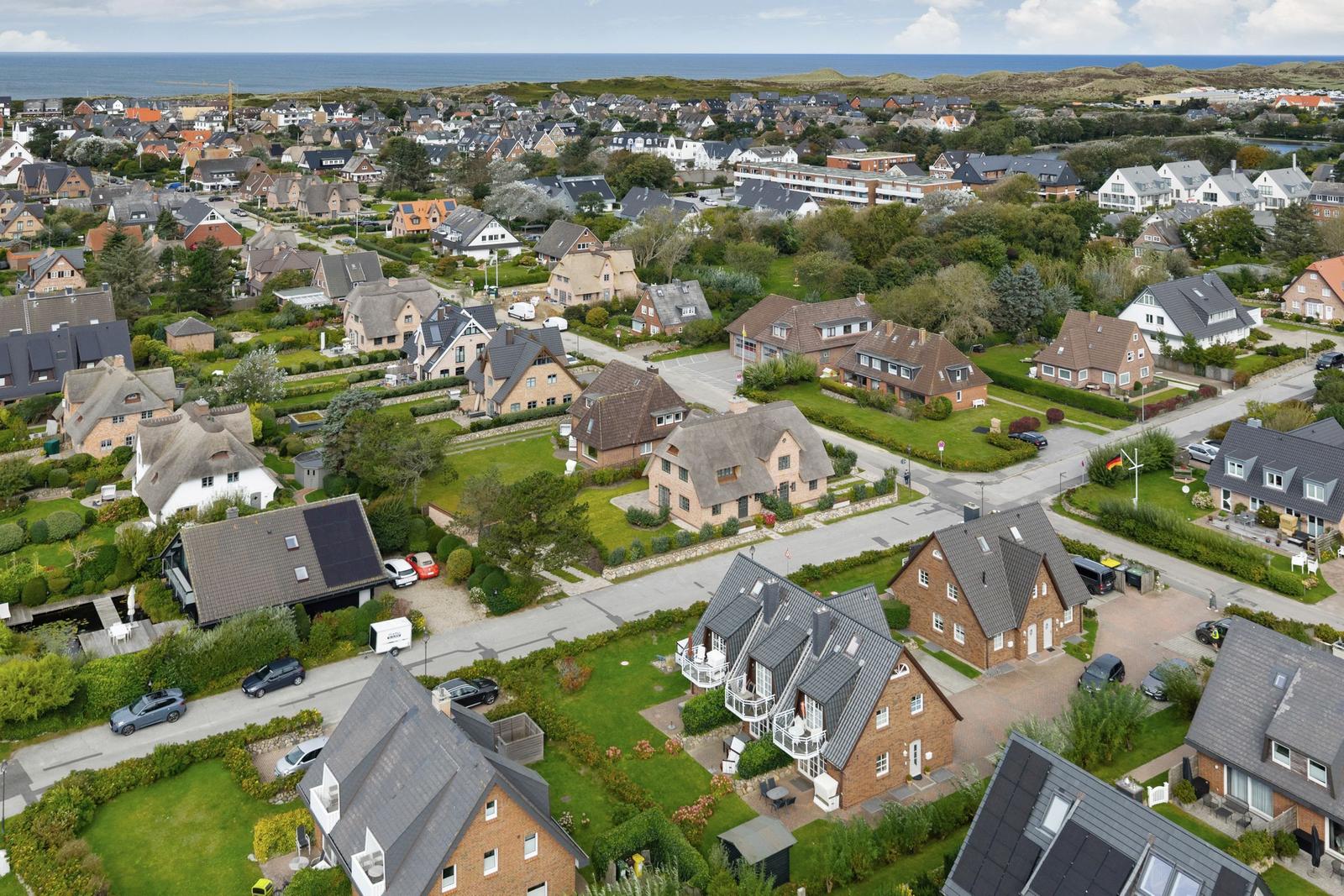 Aerial view of a coastal village with houses, gardens, and the sea in the background.