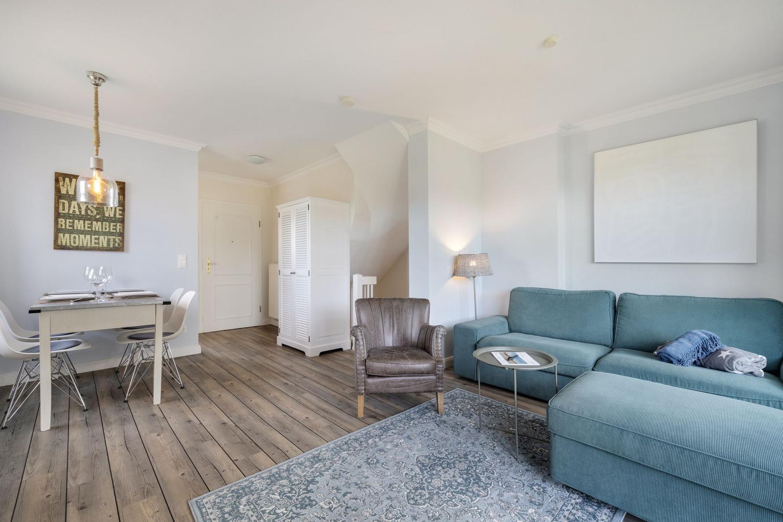 Living and dining area with blue sofa, wooden floor, and white furniture.