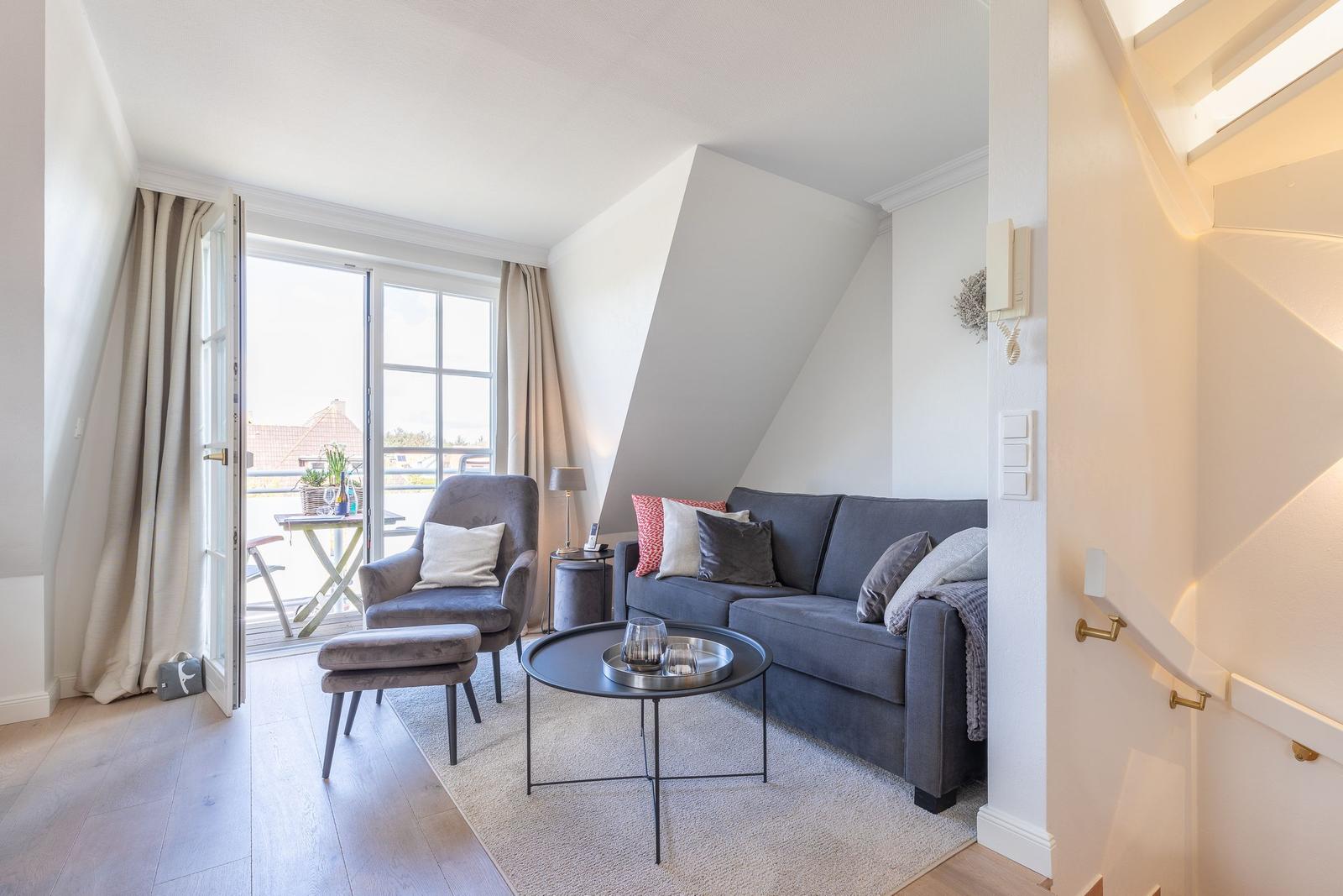 Living room with sofa, armchair, and terrace. Wooden floor and sloped ceiling.