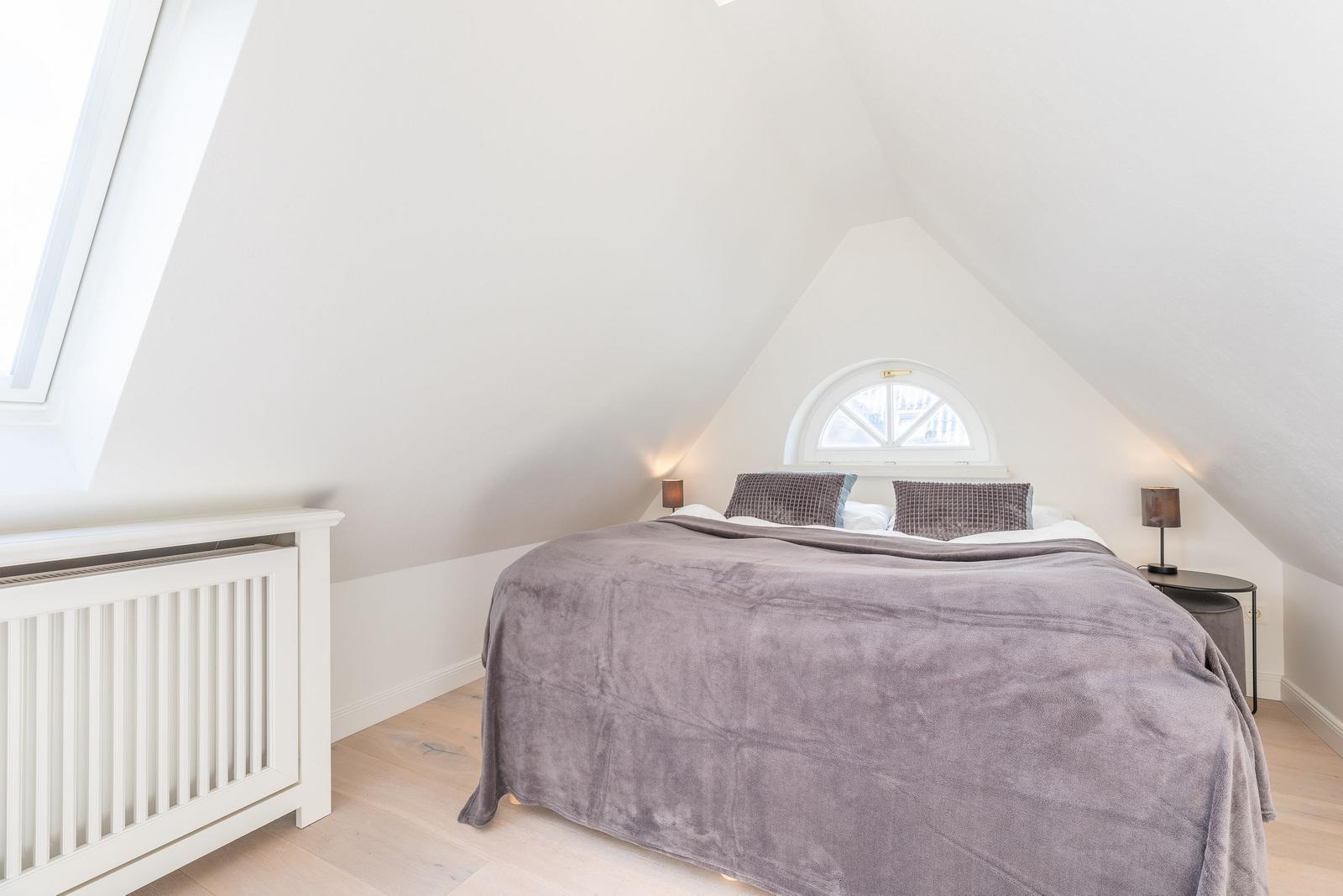 Bedroom with sloped ceiling, large bed, and window.