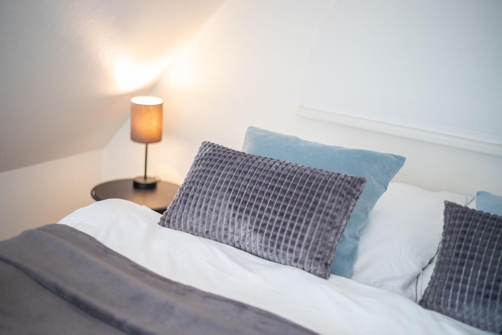 Double bed with pillows and nightstand with lamp.