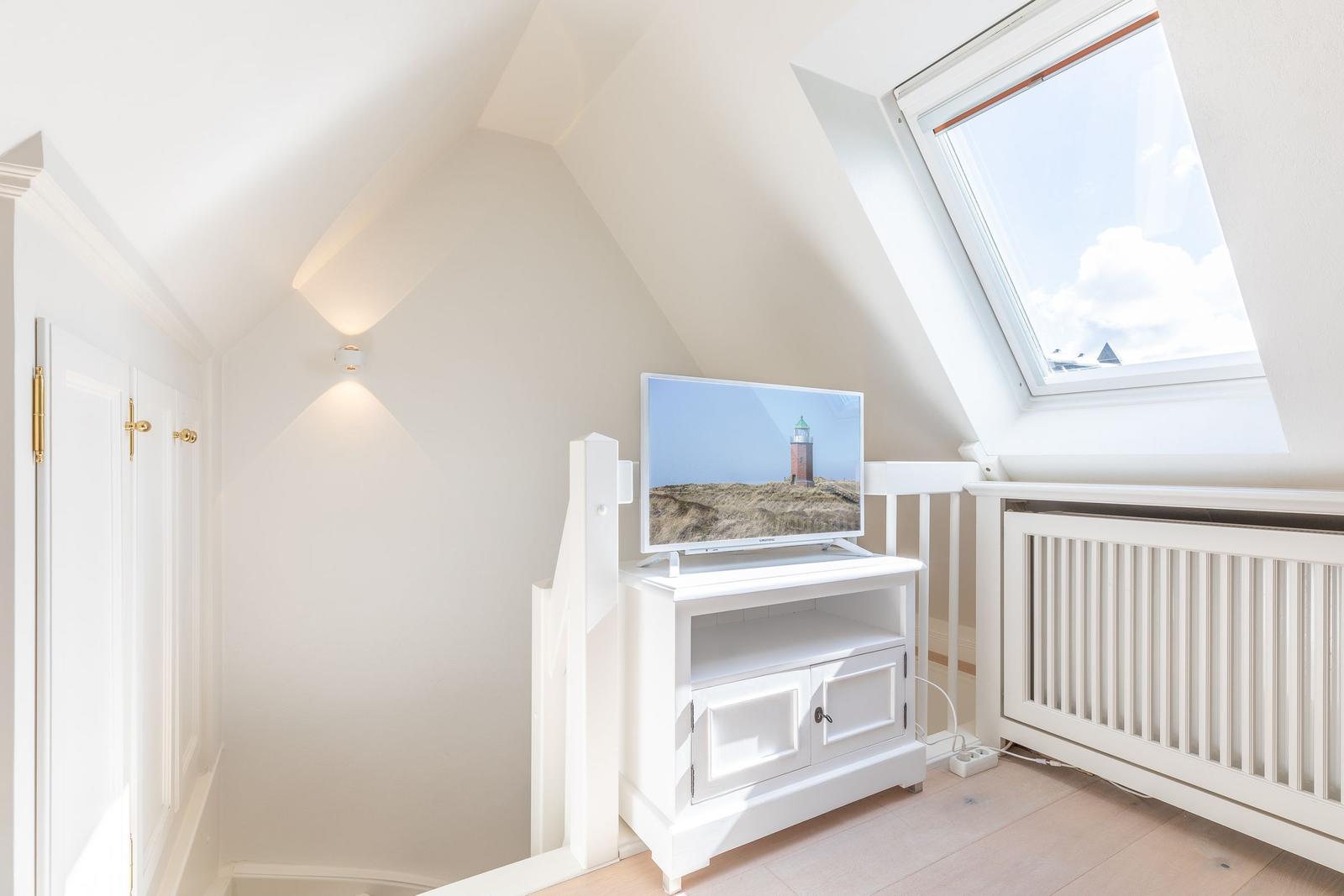 Attic room with TV and skylight. White furniture and wooden floor.