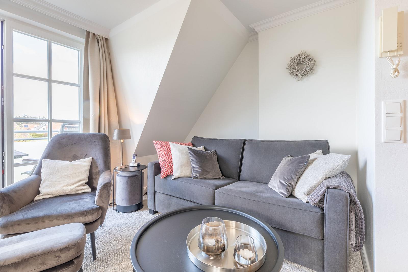 Living room with sofa, armchair, and round table under sloped ceiling.