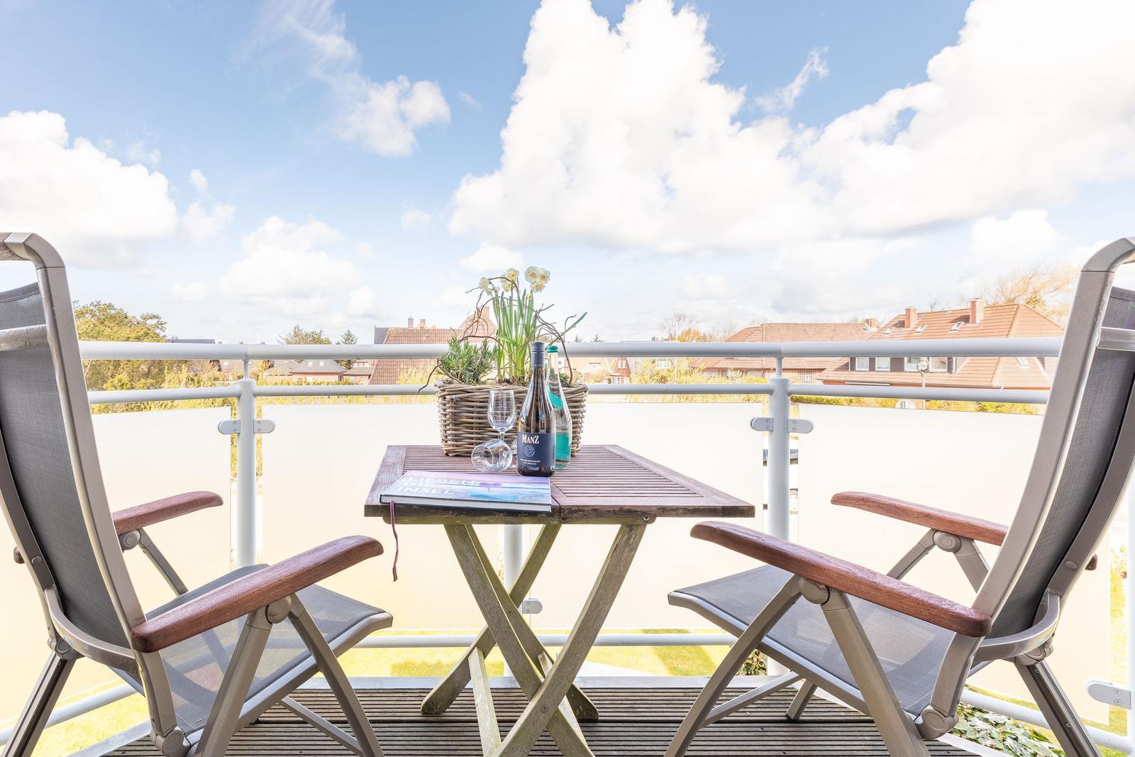 Balcony with table, two chairs, and a basket with flowers.