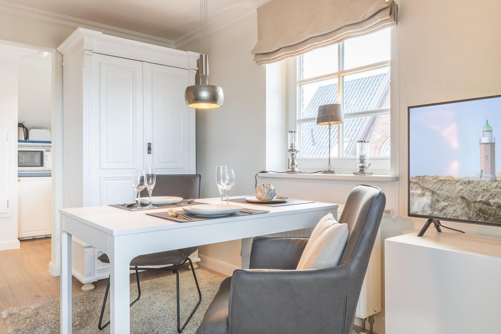 Dining area with table, chairs, and TV. Window with view of roof and tower.
