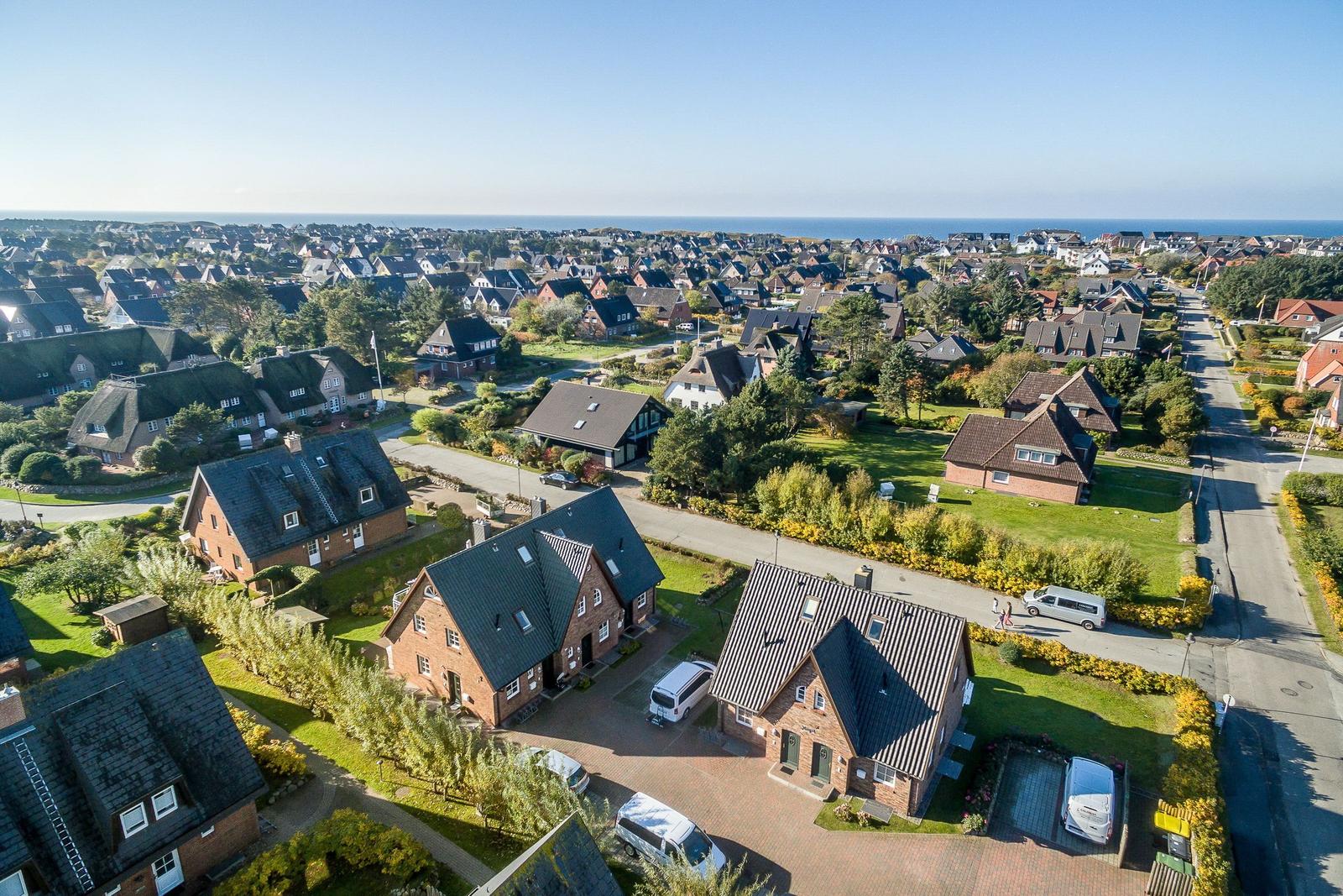 Aerial view of a coastal village with houses, gardens, and the sea in the distance.