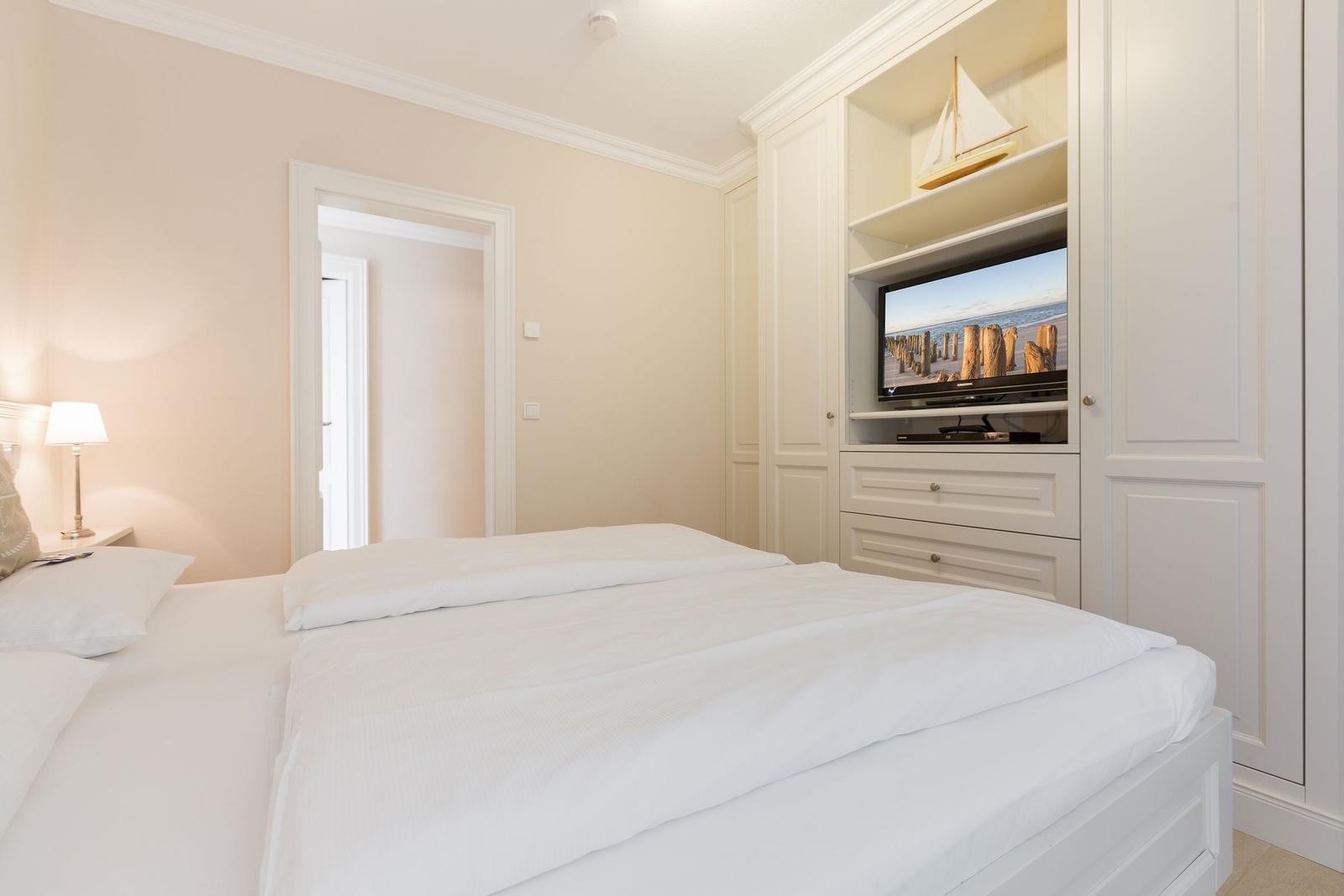 Schlafzimmer mit weißem Bett und integriertem TV-Schrank