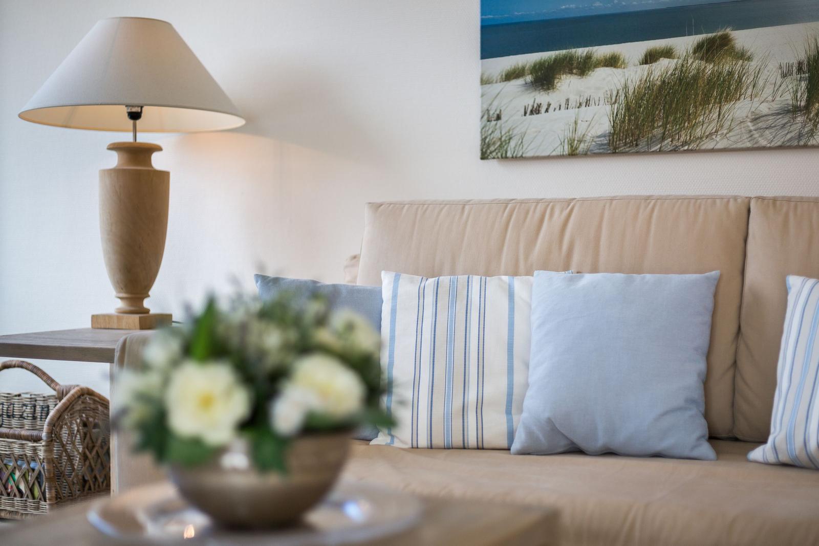 Sofa mit Kissen, Lampe und Strandbild an der Wand.