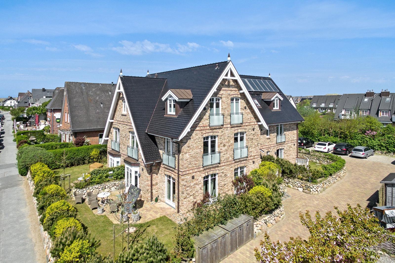 Haus mit Steinmauer, Terrasse und Garten. Mehrere Balkone und Solaranlage auf Dach.