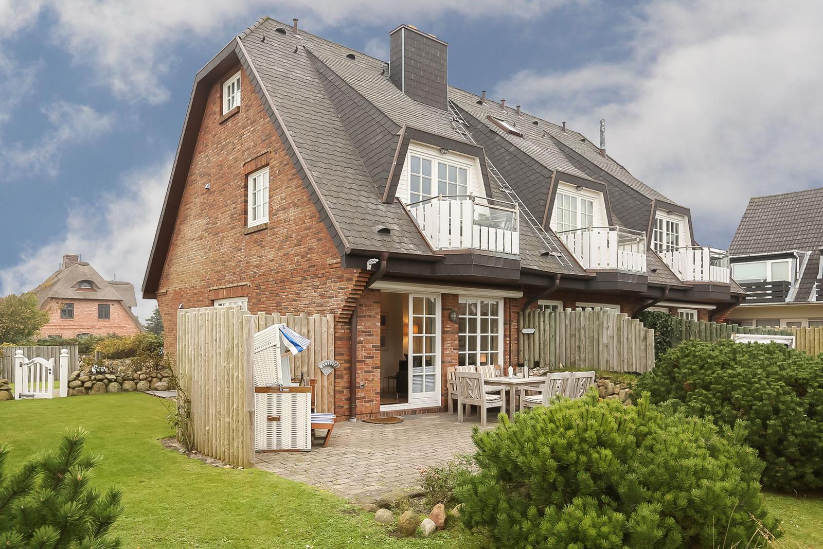 House with wooden terrace, garden patio, and green lawn.
