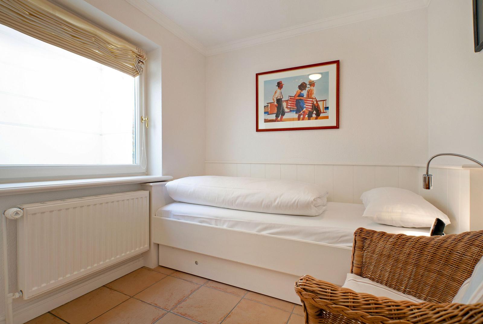 A bedroom with a white bed, window, and wicker chair.