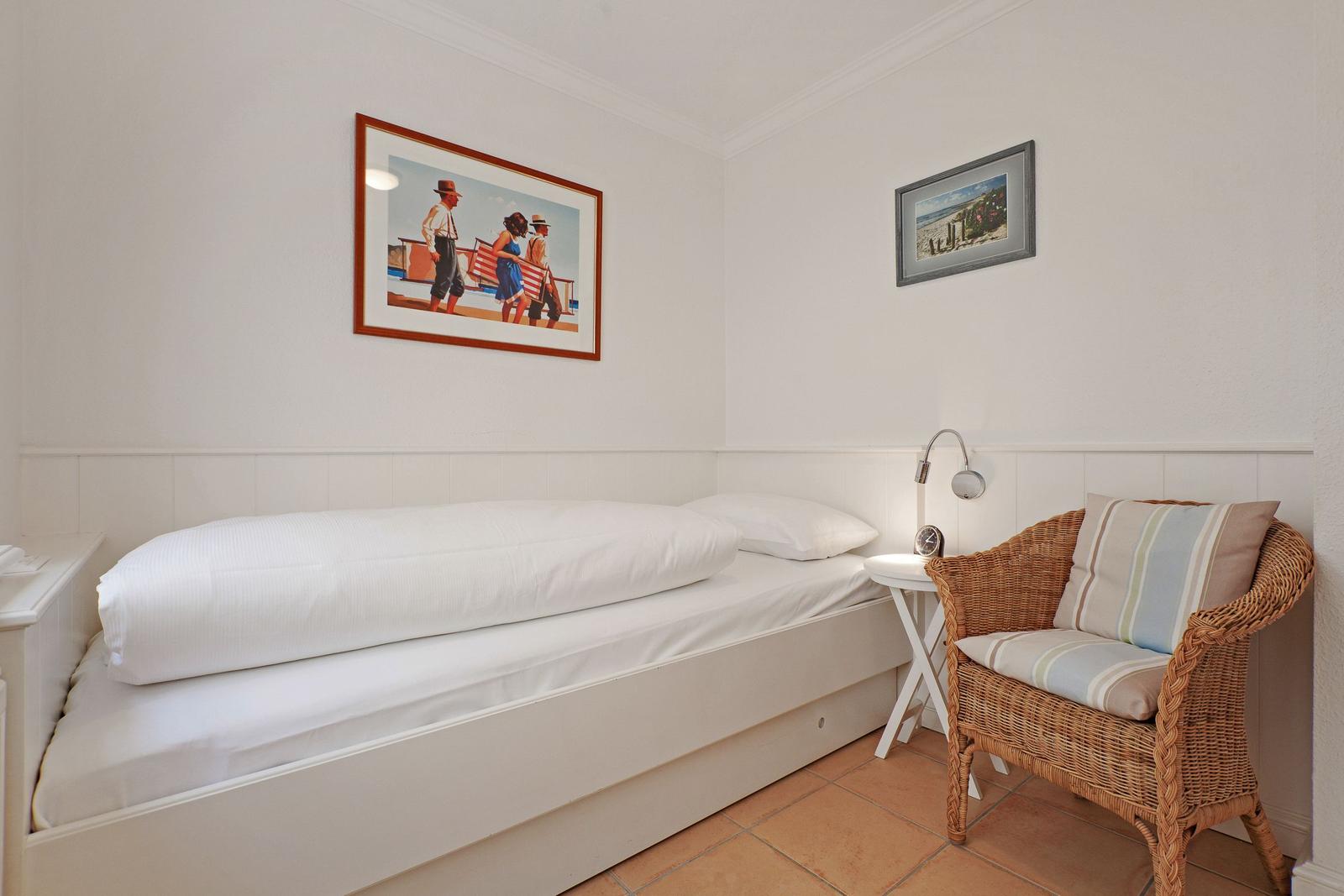 A bedroom with bed, chair, and wall pictures.