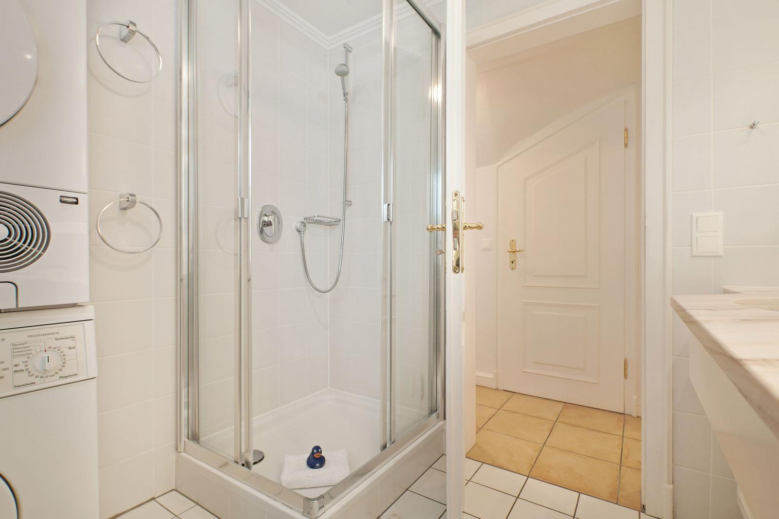 Bathroom with shower, washing machine, and sink. Door leads to living area.
