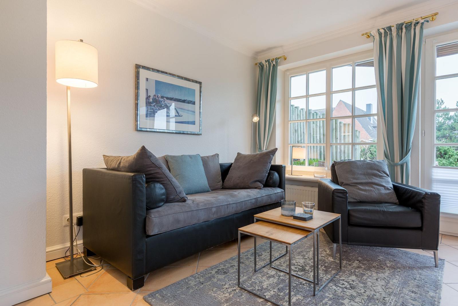 Living room with sofa, armchair, table, and windows with curtains.