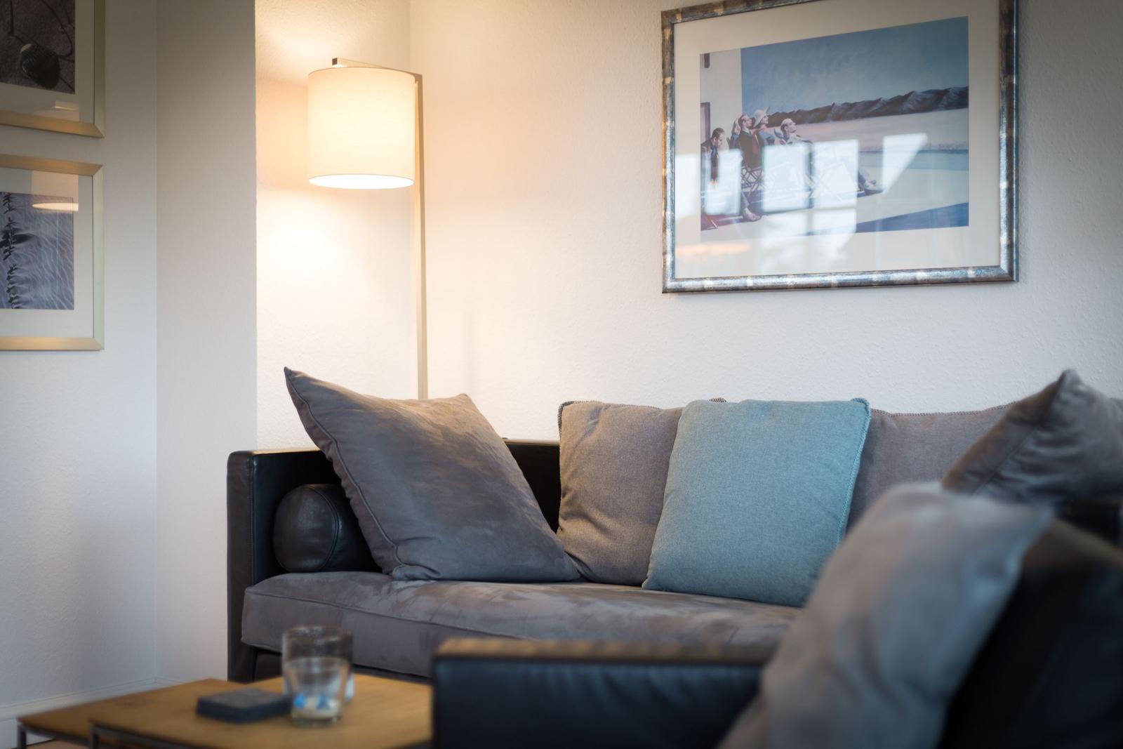 A sofa with cushions and a floor lamp on the wall.