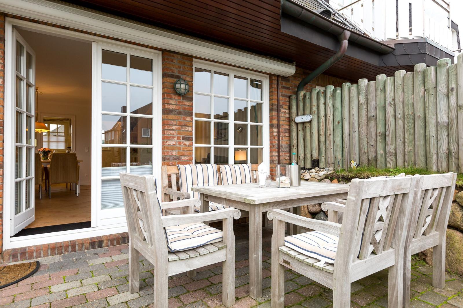 Terrace with wooden table and chairs, view into house through glass doors.