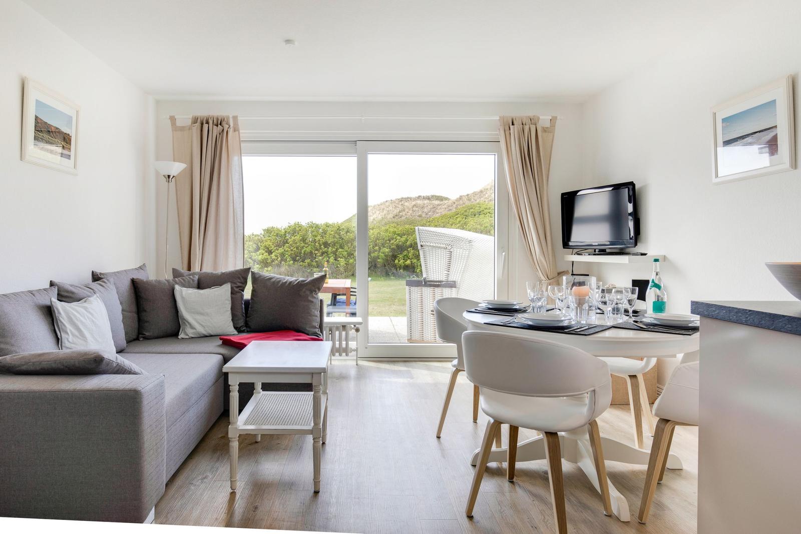 Living and dining area with sofa, table, and view of garden.