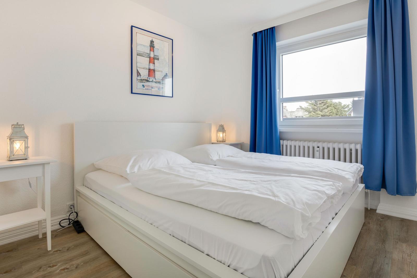 Bedroom with white bed, blue curtains, and window view.