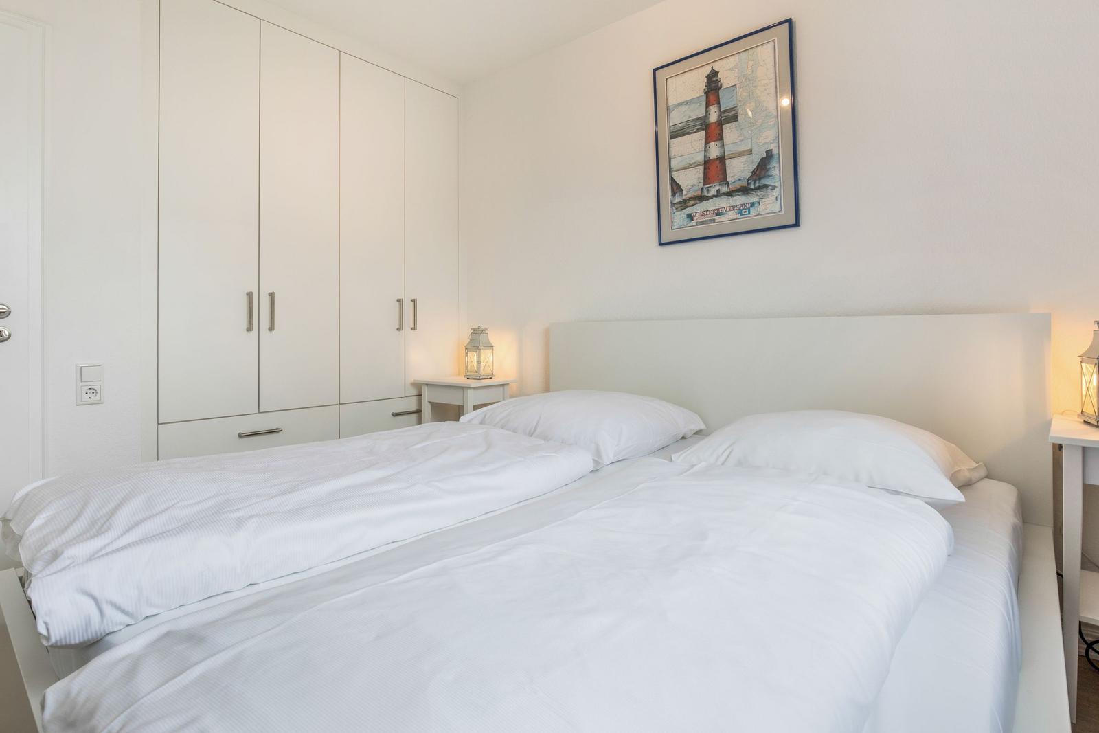 Bedroom with double bed, white walls, and wardrobe. Wall picture shows lighthouse.
