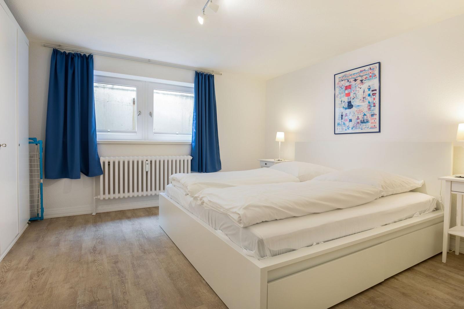 Bedroom with white bed, blue curtains, and wooden floor.