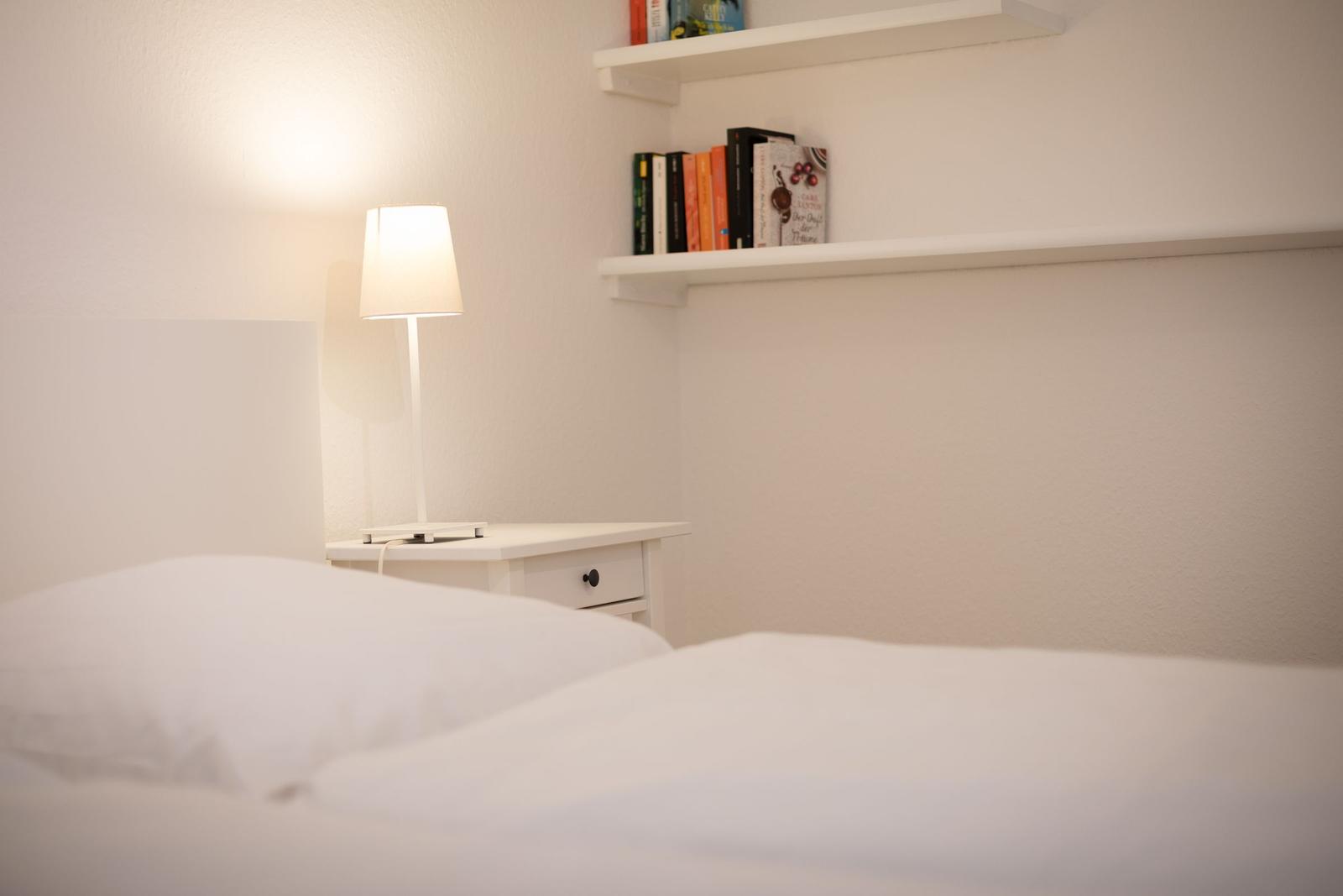 Bedroom with white bed, nightstand, and bookshelf.