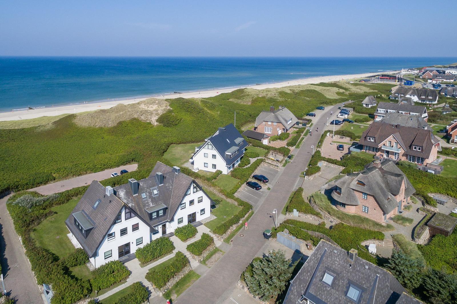 Houses near the beach with dunes and sea in the background.