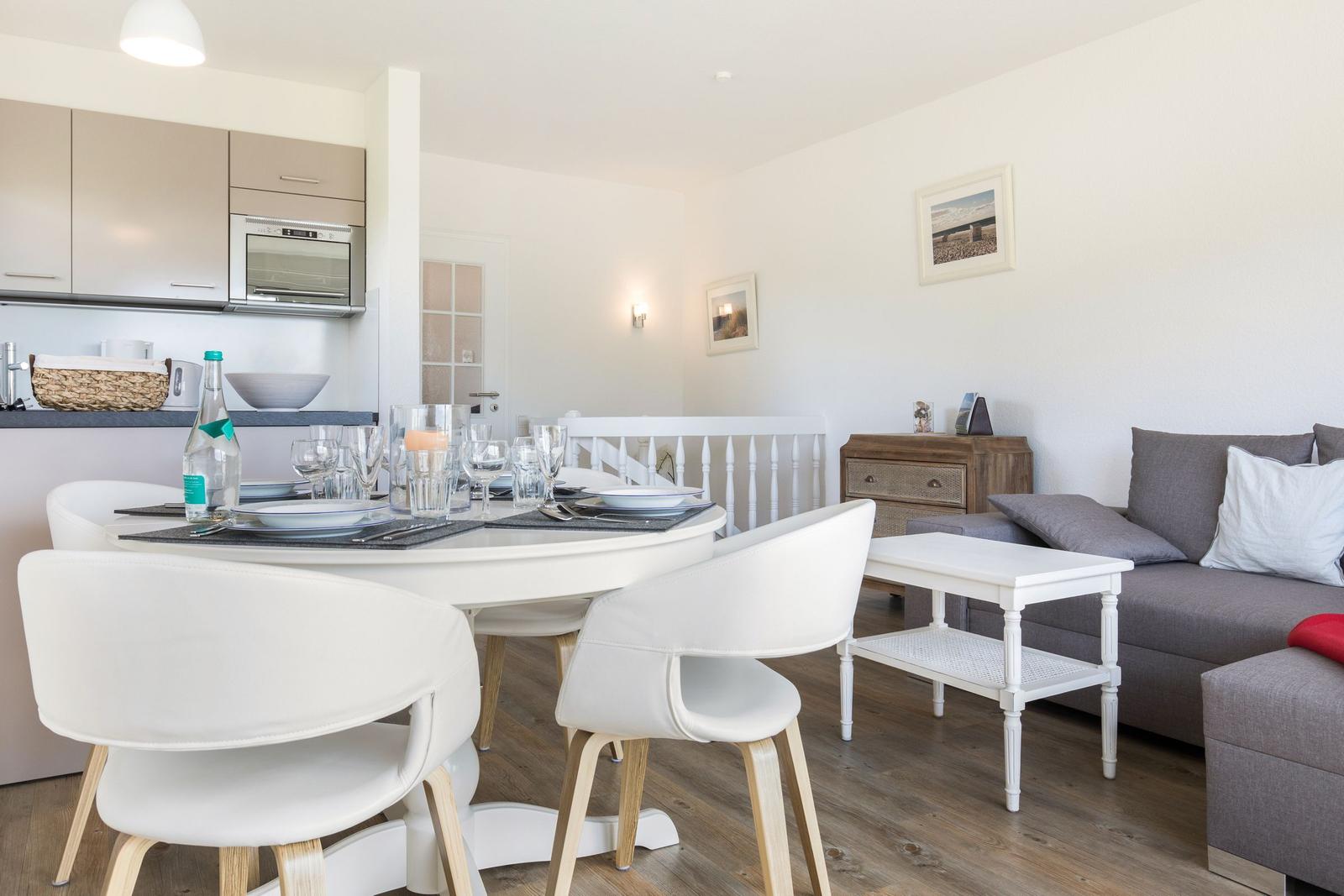 Dining area with white table and chairs, next to living area with gray sofa.