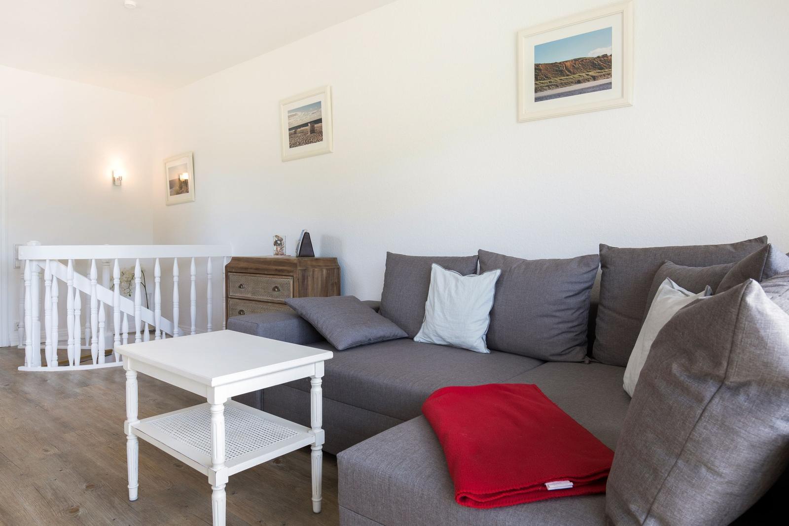 A living room with a gray sofa, white table, and pictures on the wall.