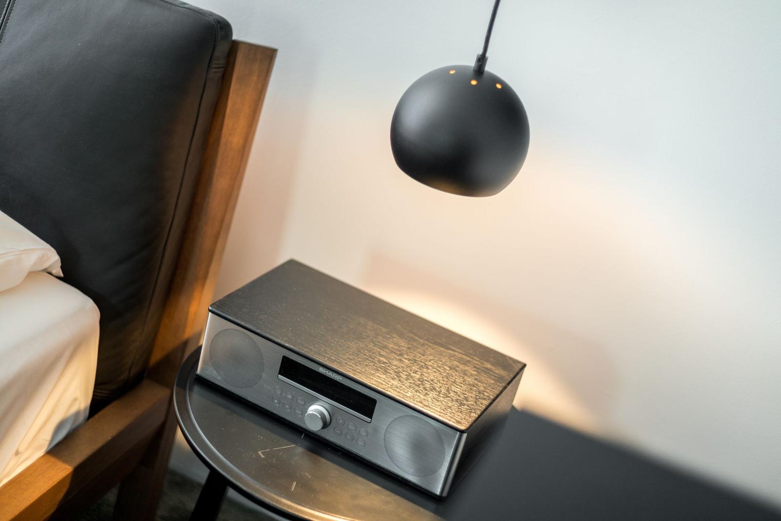 Schwarze Lampe hängt über einen Tisch mit Audio-Gerät und Bett.