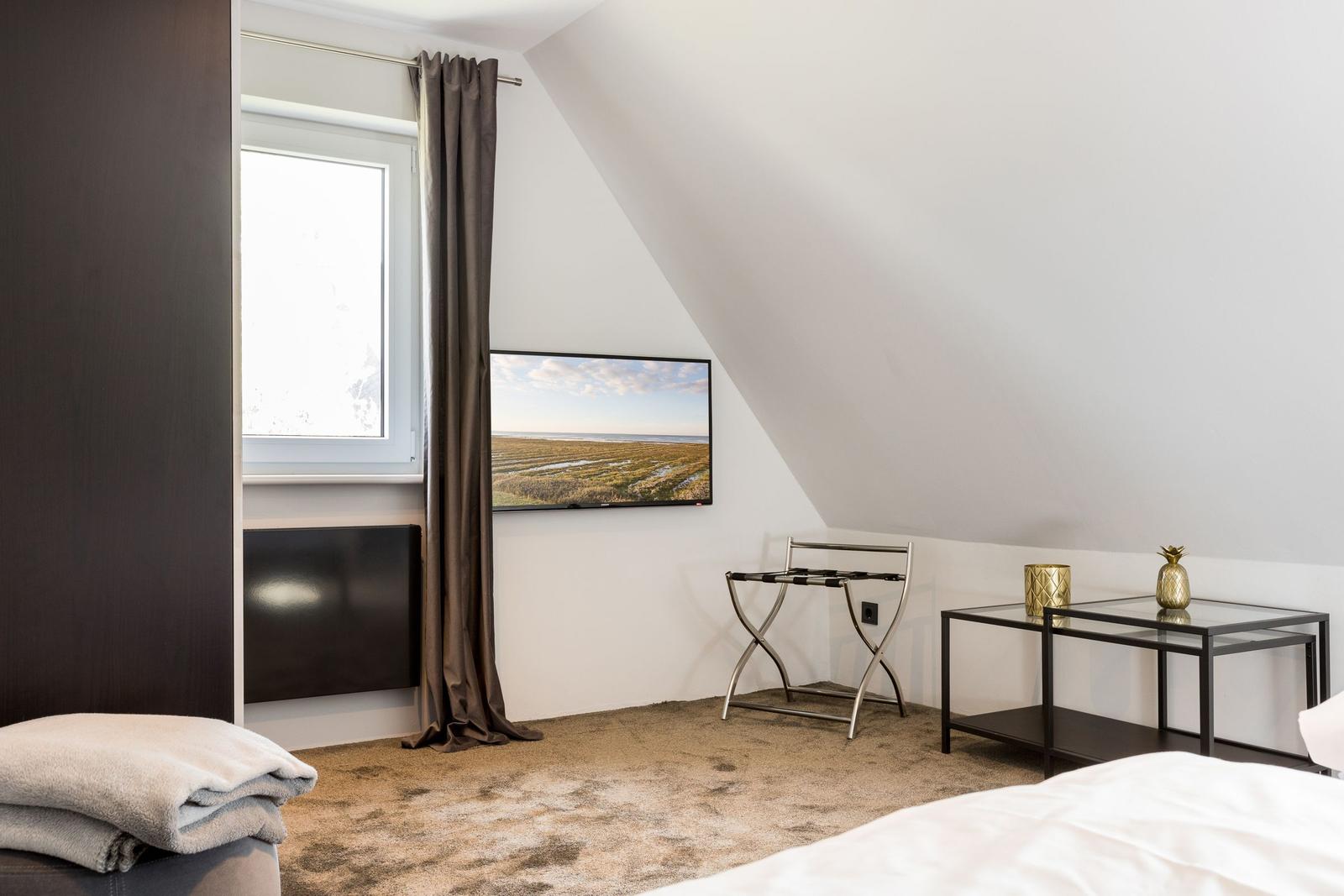 Schlafzimmer mit Dachschräge, TV, Fenster und Möbeln.