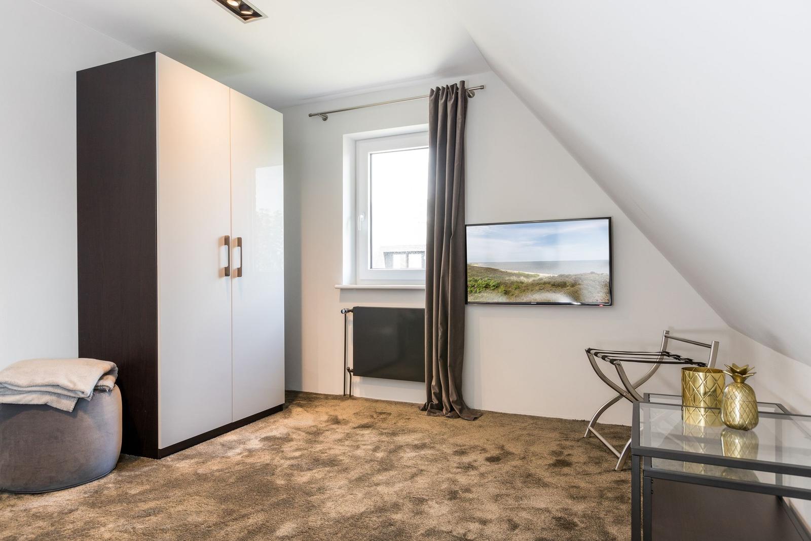 Schlafzimmer mit Kleiderschrank, Fenster, TV und Glas-Tisch.