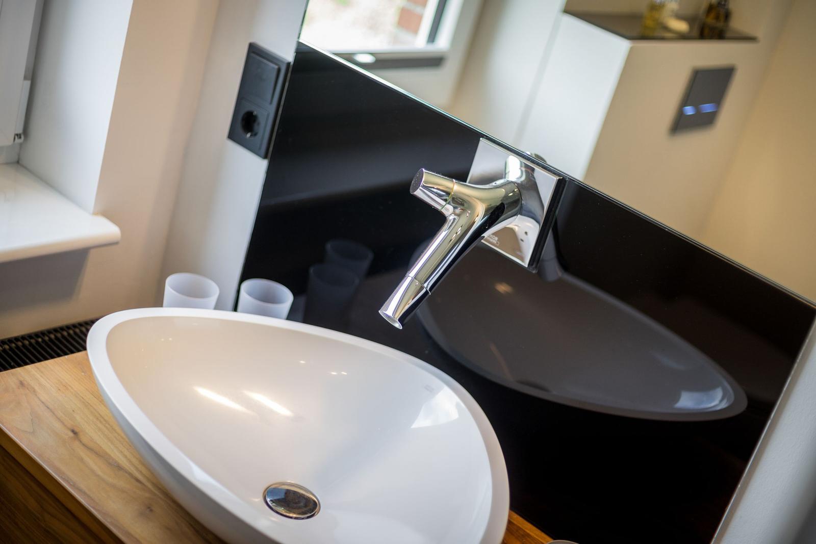 Waschbecken auf Holzplatte mit Chromarmatur und Spiegel.