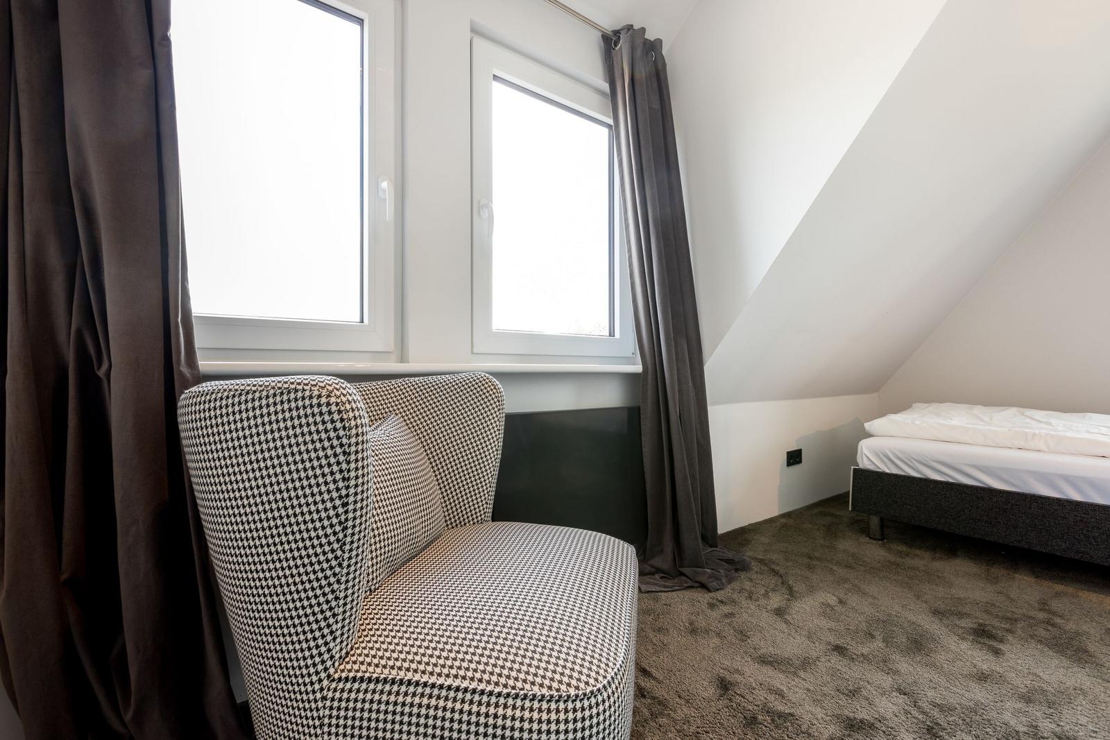 Schlafzimmer mit Dachschräge, Bett und Sessel mit kariertem Stoff.