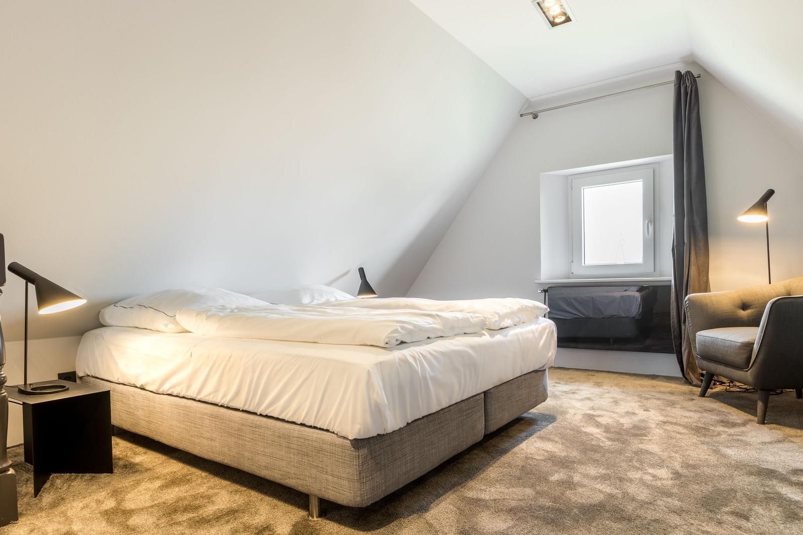 Schlafzimmer mit Doppelbett, Sessel und Fenster unter Dachschrägen.