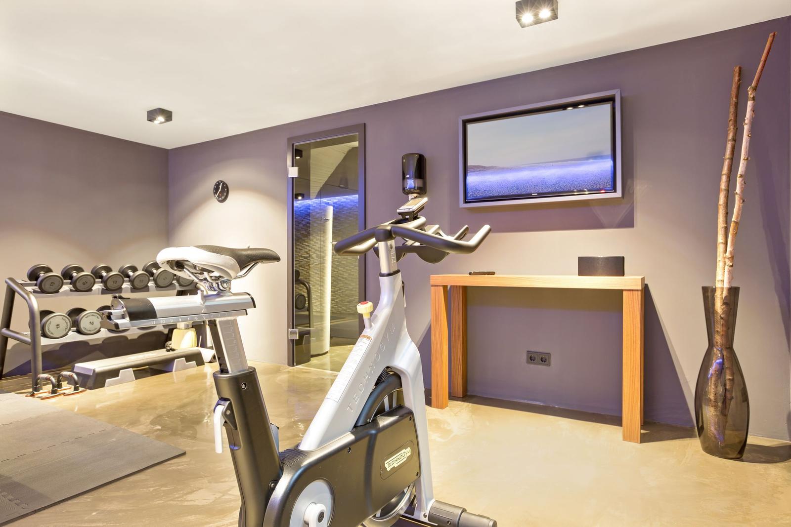 Fitnessraum mit Fahrradtrainer, Dumbbells und Fernseher an der Wand.
