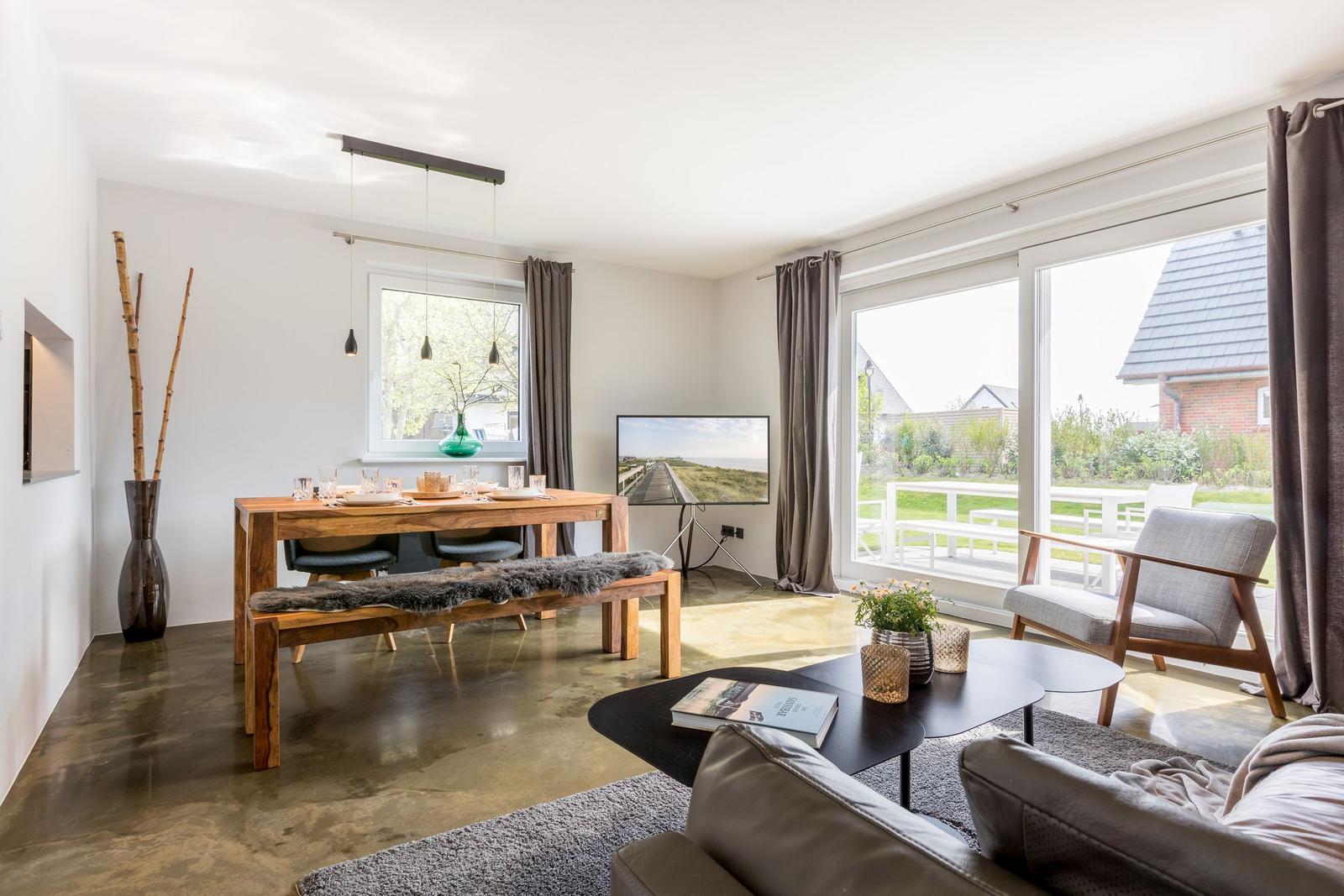 Wohn- und Essbereich mit Holztisch, Sofa und Fernseher. Durchgangstür zum Garten.