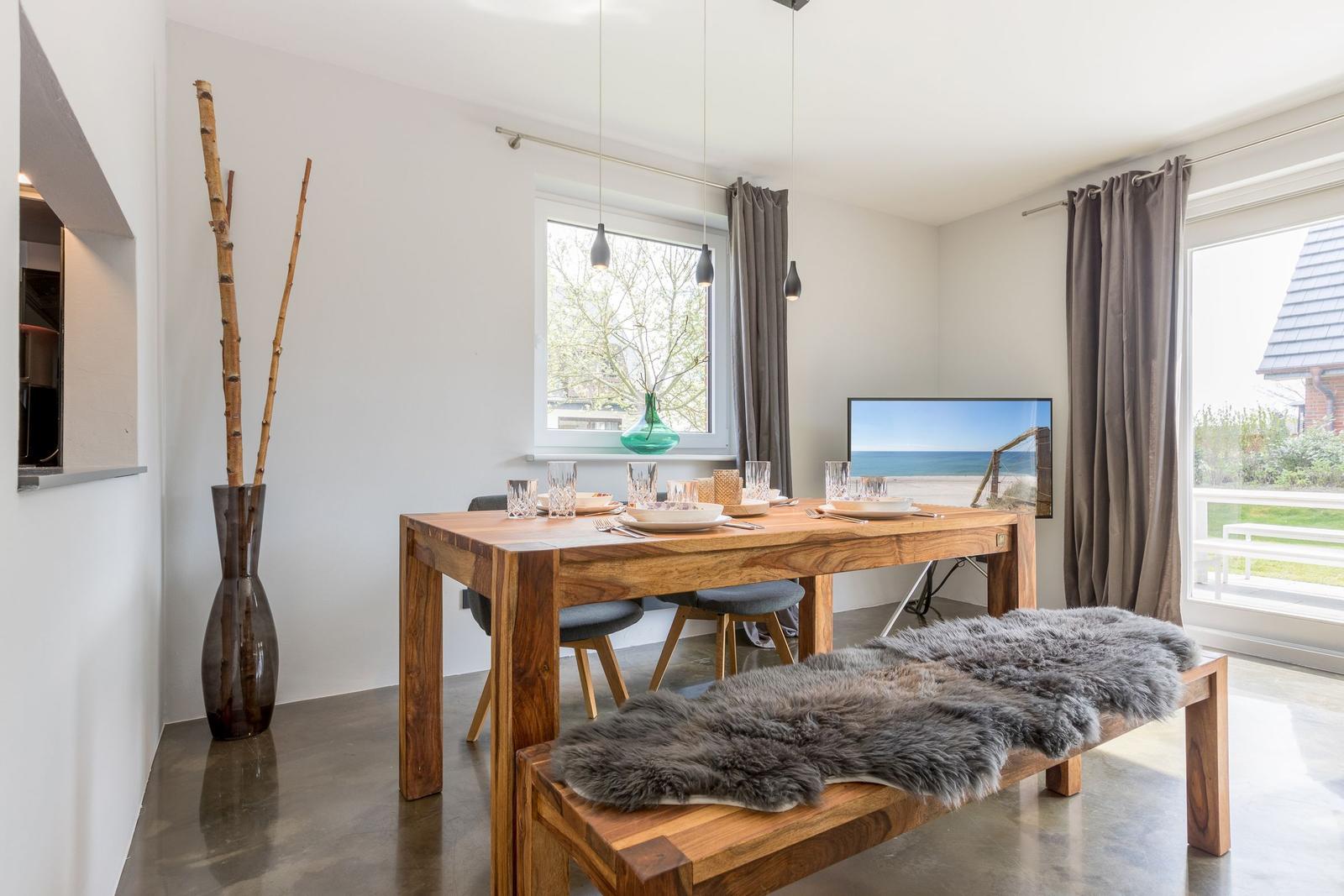 Essbereich mit Holztisch, Bänken und Fenstern. Fernseher und Vase sind sichtbar.