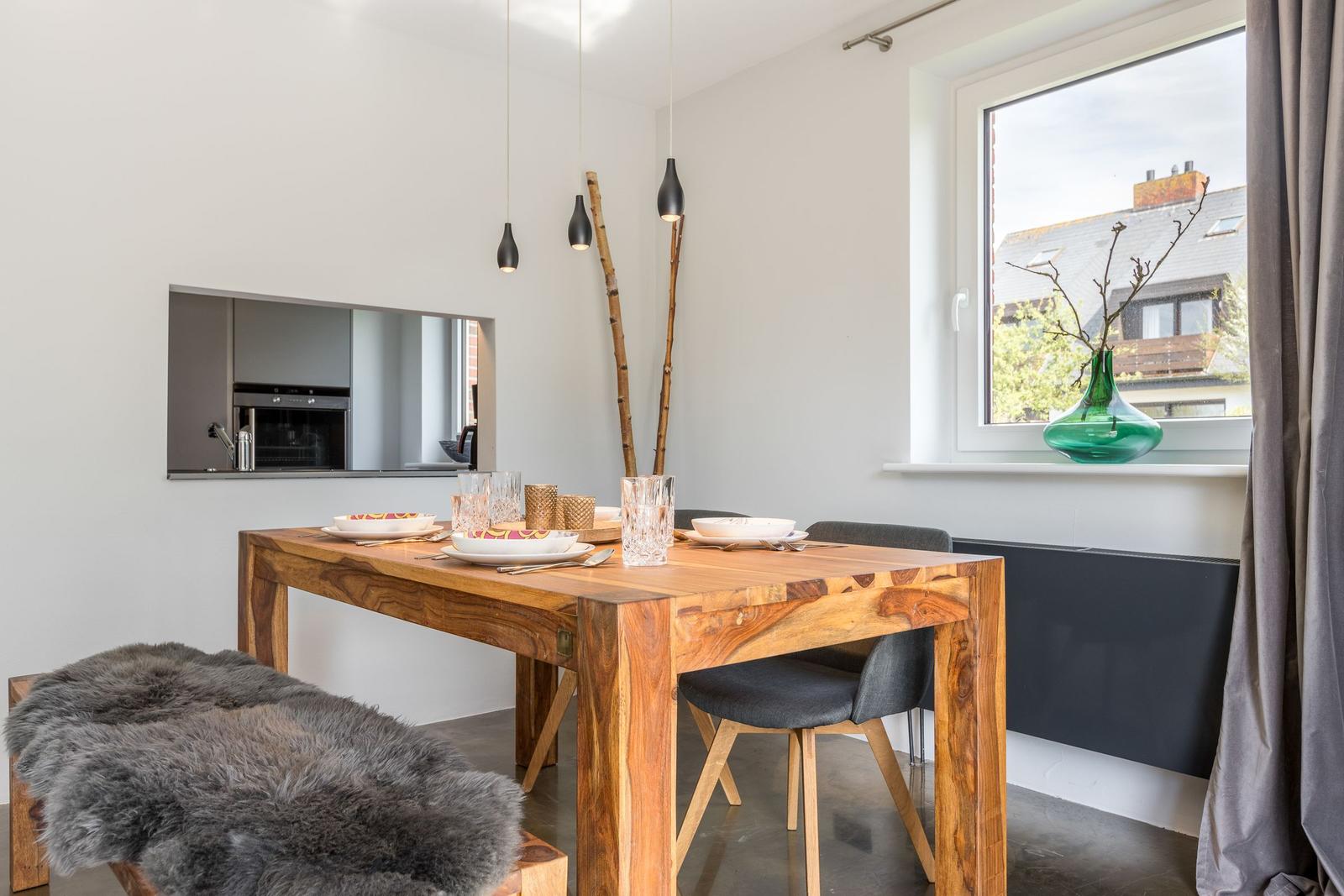 Essbereich mit Holztisch, Stühlen und Fensterblick. Auf dem Tisch stehen Geschirr und Gläser.